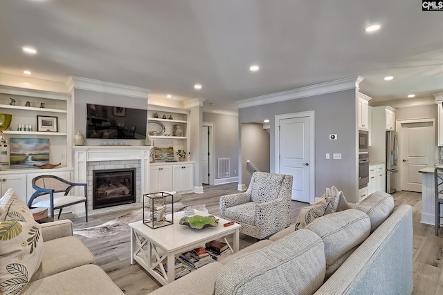 living room featuring light hardwood / wood-style flooring, ornamental molding, built in features, and a brick fireplace