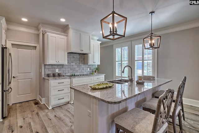 kitchen with a center island with sink, white cabinetry, stainless steel refrigerator, sink, and decorative light fixtures