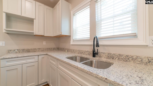 kitchen with white cabinets, light stone counters, and sink