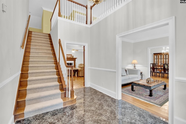 foyer featuring ceiling fan with notable chandelier, ornamental molding, dark wood-type flooring, and a high ceiling