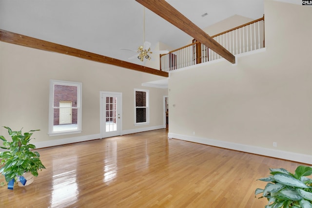 unfurnished living room featuring beam ceiling, high vaulted ceiling, light wood-type flooring, and ceiling fan