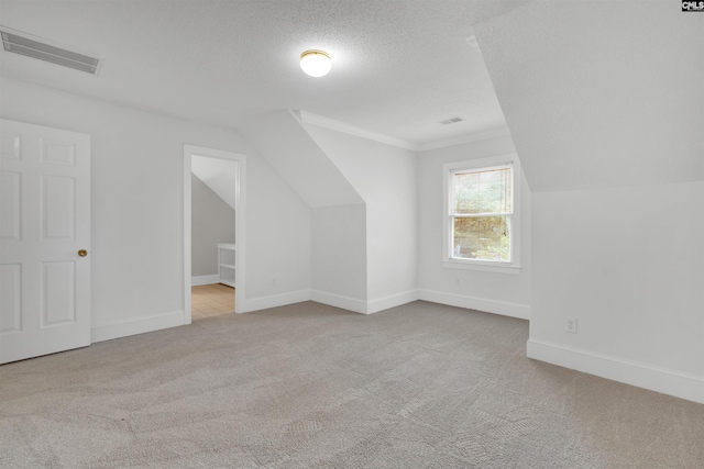 bonus room with lofted ceiling, light carpet, and a textured ceiling