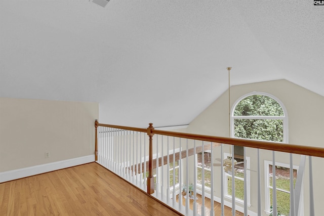 hallway featuring light hardwood / wood-style floors, a textured ceiling, and vaulted ceiling