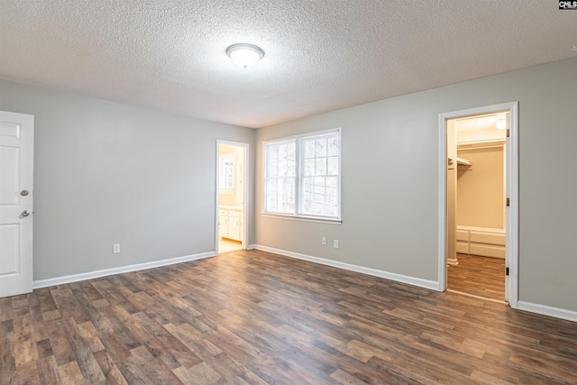 unfurnished bedroom with a closet, a walk in closet, ensuite bath, a textured ceiling, and dark hardwood / wood-style flooring