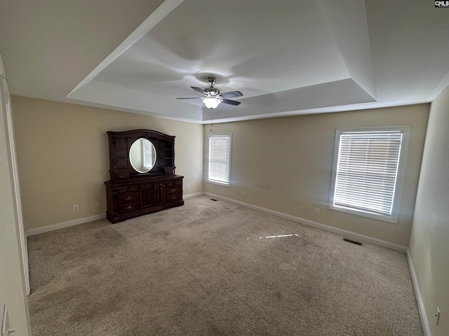 unfurnished bedroom featuring light carpet, a tray ceiling, and ceiling fan