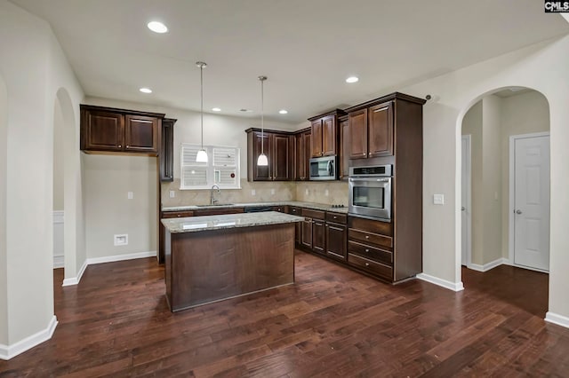 kitchen with light stone countertops, sink, a kitchen island, stainless steel appliances, and pendant lighting