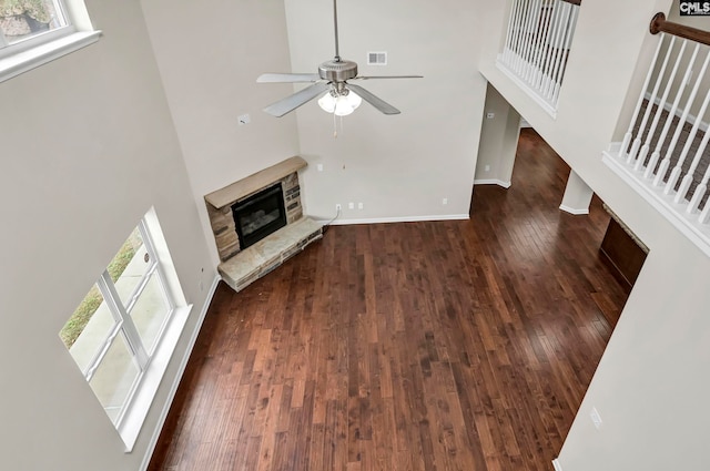 unfurnished living room featuring dark wood-type flooring, ceiling fan, a towering ceiling, and a fireplace