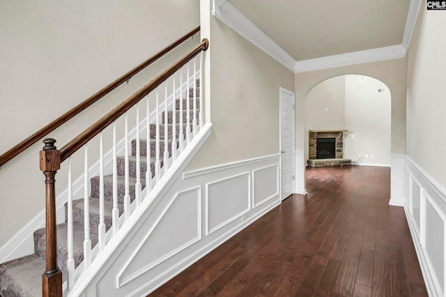 staircase with ornamental molding, a stone fireplace, and hardwood / wood-style flooring