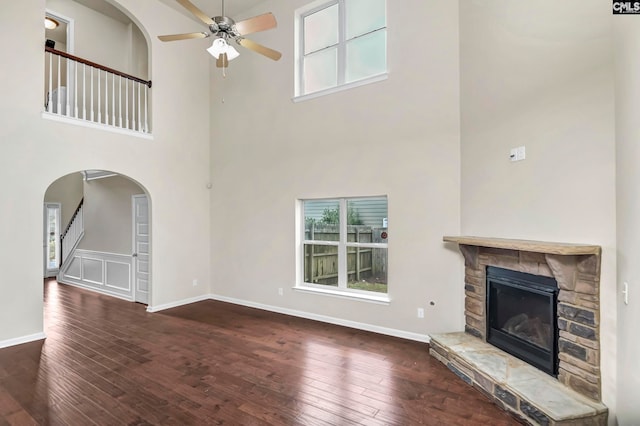 unfurnished living room with a high ceiling, ceiling fan, a stone fireplace, and dark hardwood / wood-style flooring