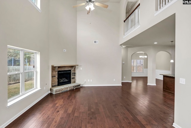 unfurnished living room featuring ceiling fan, a stone fireplace, a high ceiling, and dark hardwood / wood-style flooring