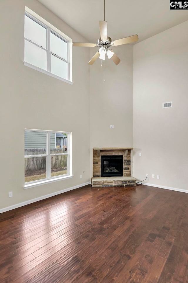 unfurnished living room featuring a high ceiling, dark hardwood / wood-style flooring, a fireplace, and ceiling fan