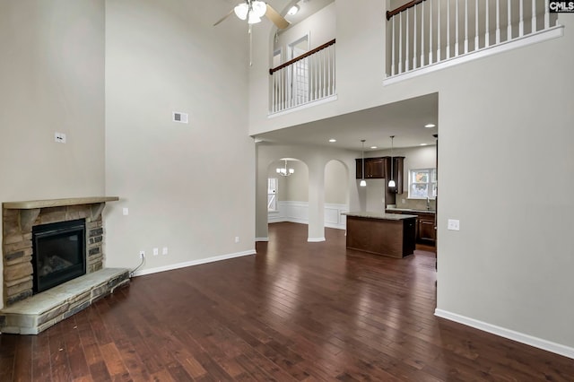 unfurnished living room with ceiling fan, a fireplace, a towering ceiling, and dark hardwood / wood-style flooring