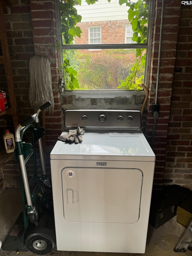 clothes washing area with washer / clothes dryer and brick wall