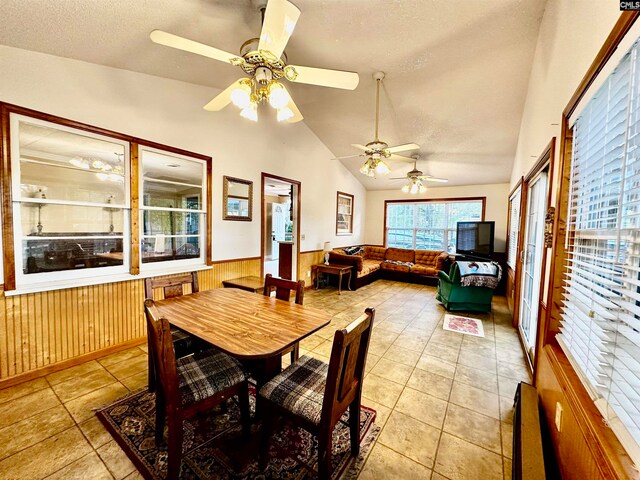 tiled dining room with vaulted ceiling, ceiling fan, a textured ceiling, and wood walls