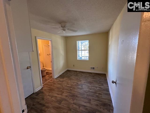 unfurnished bedroom featuring dark wood-type flooring, ensuite bath, a textured ceiling, and ceiling fan