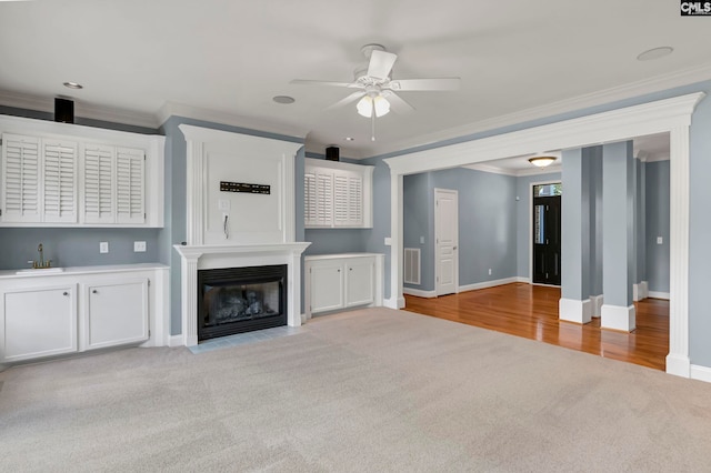 unfurnished living room featuring light carpet, crown molding, sink, and ceiling fan