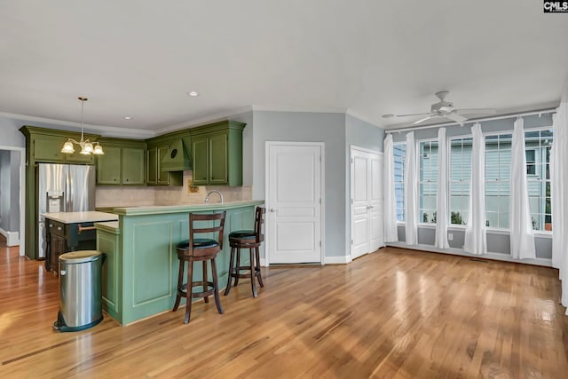 kitchen with hanging light fixtures, light hardwood / wood-style flooring, custom range hood, ceiling fan with notable chandelier, and green cabinetry