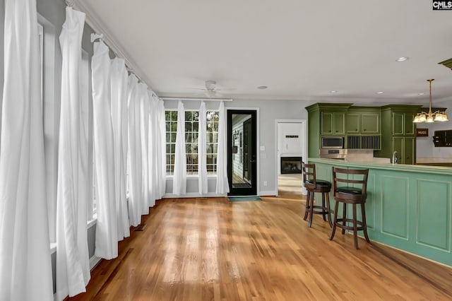 kitchen with stainless steel microwave, light hardwood / wood-style flooring, green cabinetry, pendant lighting, and ceiling fan with notable chandelier