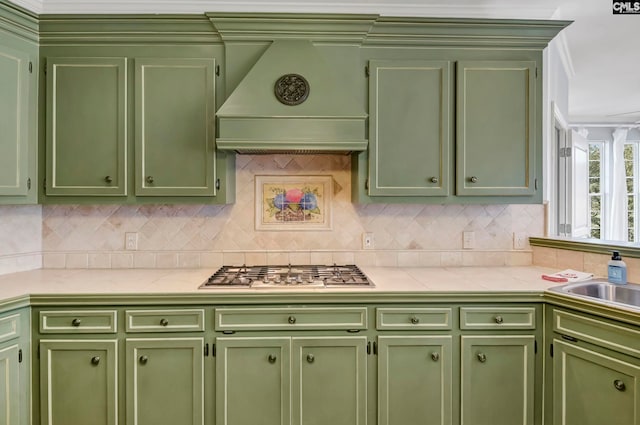 kitchen featuring stainless steel gas cooktop, decorative backsplash, sink, and premium range hood