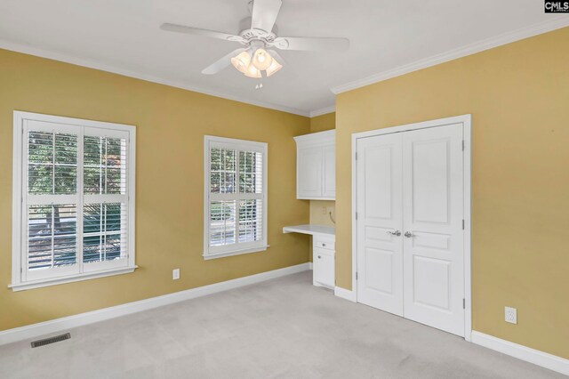 unfurnished bedroom featuring a closet, built in desk, light carpet, crown molding, and ceiling fan