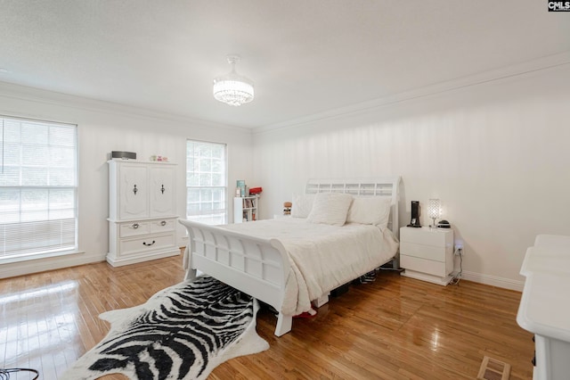 bedroom featuring ornamental molding, light hardwood / wood-style flooring, and multiple windows