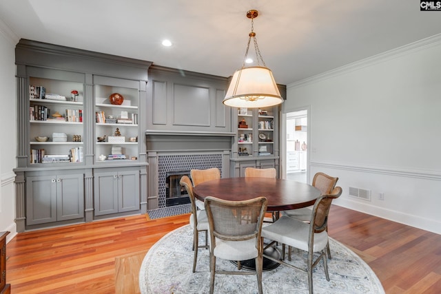 dining room featuring built in features, light hardwood / wood-style flooring, ornamental molding, and a tile fireplace