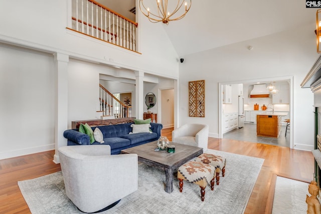 living room featuring an inviting chandelier, a towering ceiling, sink, and light hardwood / wood-style floors