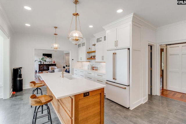 kitchen featuring built in fridge, white cabinetry, a kitchen breakfast bar, ornamental molding, and a center island with sink