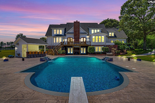 pool at dusk with a patio area, pool water feature, and exterior bar