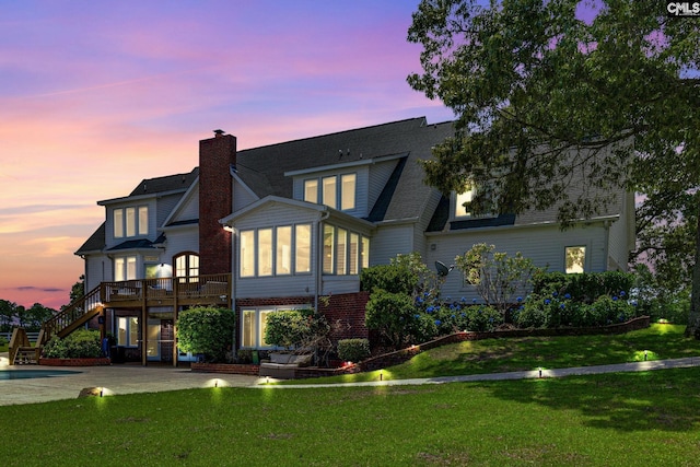 back house at dusk featuring a patio and a lawn