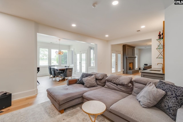 living room with sink, a large fireplace, light hardwood / wood-style floors, and french doors