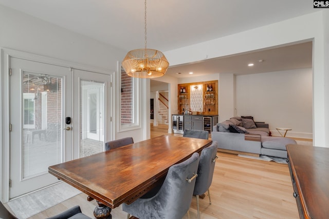 dining area with light hardwood / wood-style flooring, an inviting chandelier, beverage cooler, bar area, and french doors