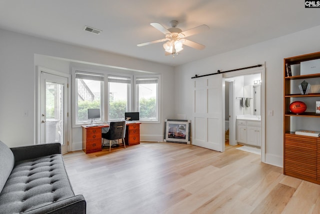 office space featuring ceiling fan, a barn door, and light hardwood / wood-style floors