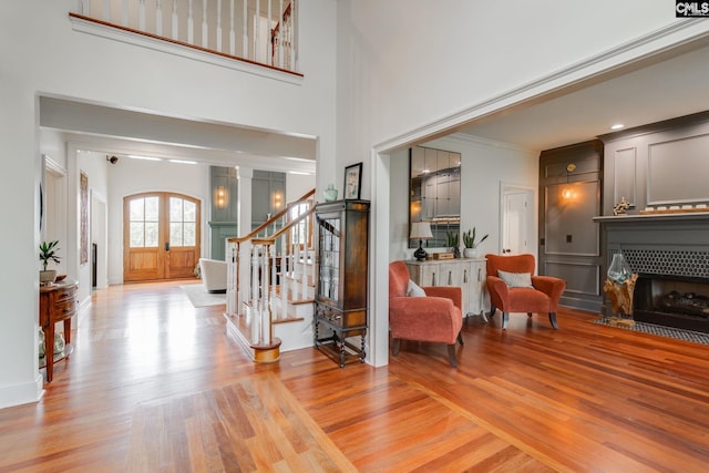 foyer entrance featuring a tiled fireplace, a high ceiling, crown molding, light wood-type flooring, and french doors