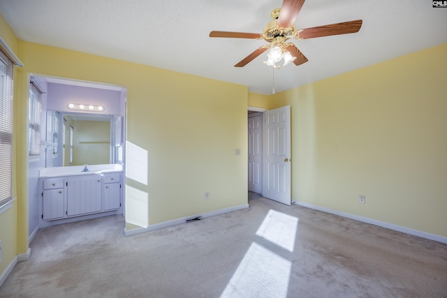 unfurnished bedroom with light colored carpet, connected bathroom, sink, and ceiling fan