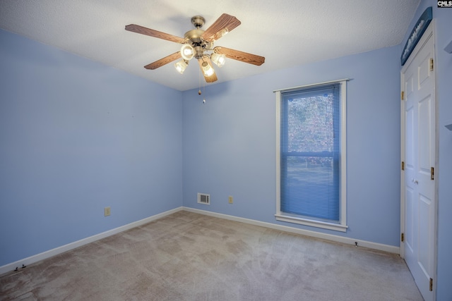 empty room featuring ceiling fan, a textured ceiling, and light colored carpet