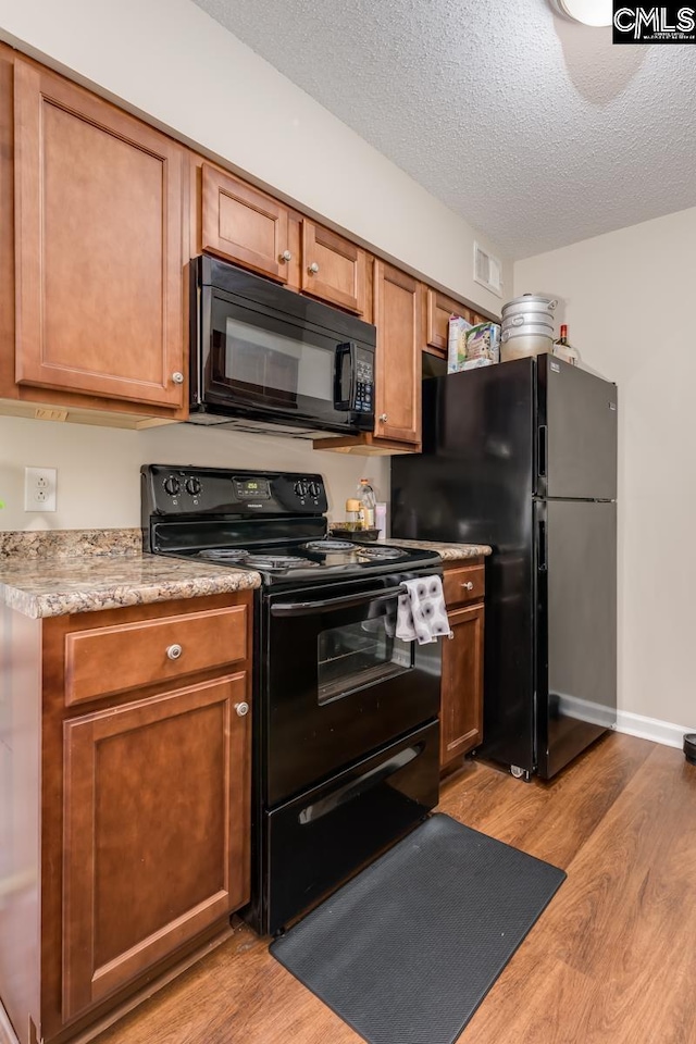 kitchen with a textured ceiling, black appliances, and light hardwood / wood-style flooring