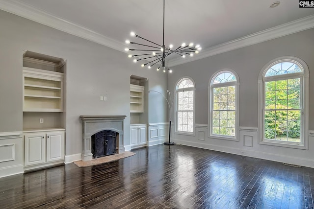 unfurnished living room featuring ornamental molding, built in shelves, an inviting chandelier, and dark hardwood / wood-style flooring