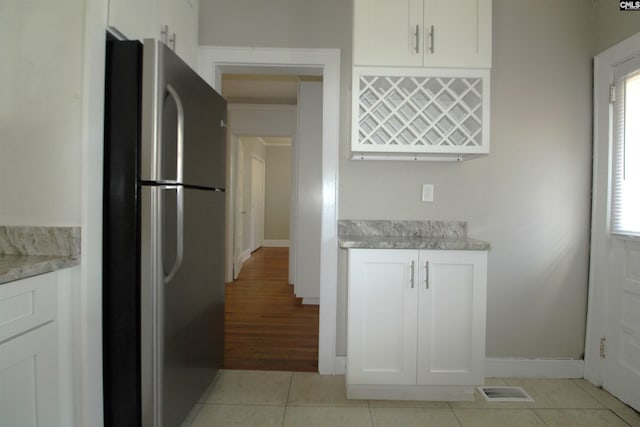 kitchen with white cabinets, a healthy amount of sunlight, light tile patterned flooring, and stainless steel fridge