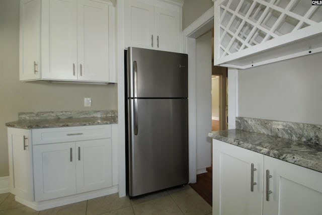 kitchen with white cabinetry, stainless steel fridge, light stone counters, and light tile patterned floors