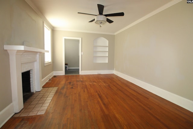 unfurnished living room with a tiled fireplace, crown molding, wood-type flooring, and built in shelves