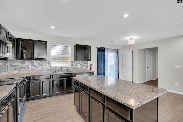 kitchen with decorative backsplash, a kitchen island, a sink, stainless steel appliances, and light wood-style flooring