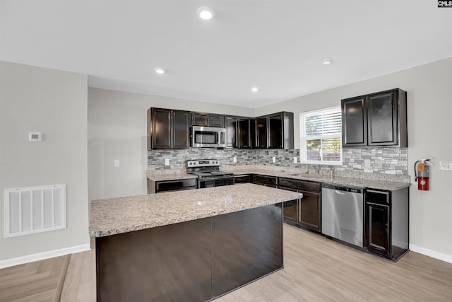 kitchen featuring decorative backsplash, dark brown cabinets, stainless steel appliances, light hardwood / wood-style floors, and a center island