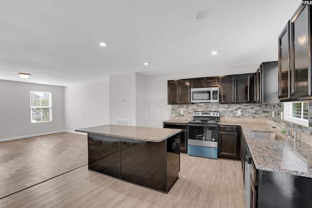 kitchen with decorative backsplash, light wood-type flooring, stainless steel appliances, sink, and a center island