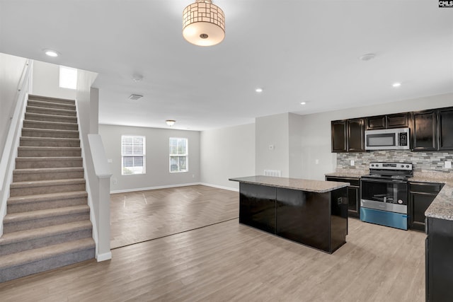 kitchen featuring tasteful backsplash, light stone countertops, a center island, light hardwood / wood-style floors, and stainless steel appliances