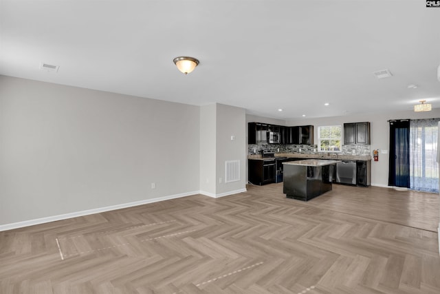 kitchen with appliances with stainless steel finishes, backsplash, open floor plan, a kitchen island, and visible vents