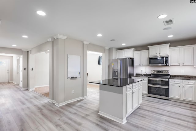 kitchen with white cabinets, light hardwood / wood-style flooring, stainless steel appliances, ornate columns, and a center island