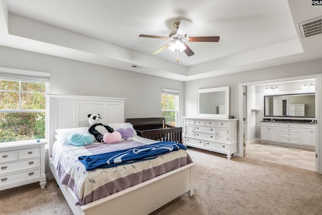 carpeted bedroom with ensuite bath, a raised ceiling, and ceiling fan