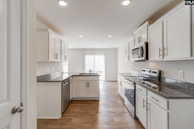 kitchen featuring kitchen peninsula, white cabinets, dark wood-type flooring, sink, and stainless steel appliances