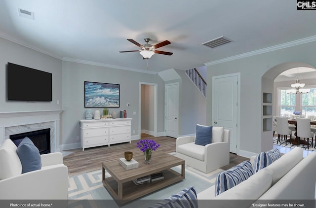 living room with crown molding, hardwood / wood-style floors, a fireplace, and ceiling fan with notable chandelier